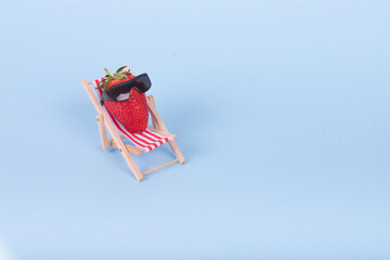 Creative  idea made of deck chair, sun umbrella and strawberry with sunglasses on a pastel blue...