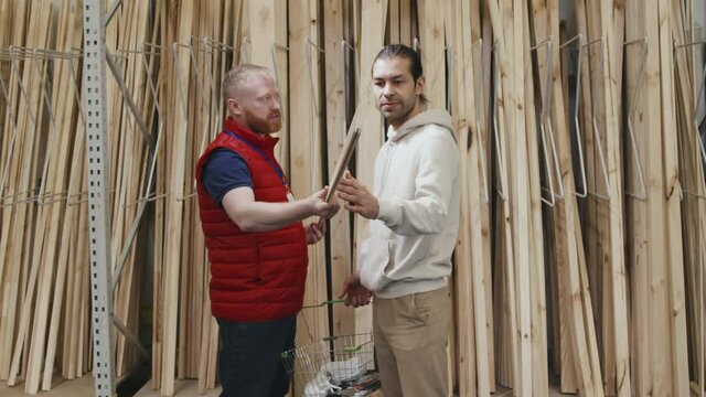 Slowmo shot of male hardware store worker in puffy vest showing siding panel to customer and giving advice