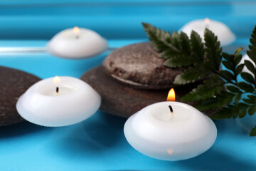 Fototapeta na wymiar Burning candles, green leaf and spa stones in water