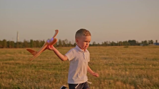 Happy blonde-haired child runs with toy airplane at sunset on meadow field. Kid dreams of becoming an astronaut pilot. Child dream is to run around with toy. Child is an airplane pilot. Dream Concept.