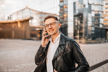 Handsome man with glasses with a smartphone on the street of a big city. Businessman talking on the phone on urban background