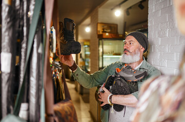 Bearded male hunter choosing boots in gun store