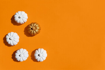 Glamorous Halloween concept. White and gold pumpkins on an orange background. Top view. Copy space.