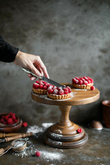 Sand baskets with custard and raspberries on a high wooden stand. Summer pastries with fresh seasonal berries.