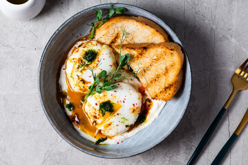 Cilbir or Turkish Eggs. dish served as mezze: poached eggs topped over herbed greek yogurt, then drizzled with hot spiced paprika olive oil. Turkish breakfast in a grey bowl on marble background