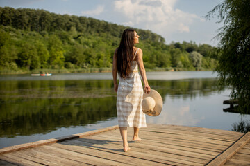 Relaxing young woman standing on wooden pier at the lake