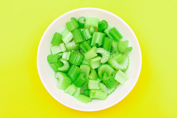 Fresh Chopped Celery Pieces with Water Drops in White Bowl on Yellow Background. Vegan and Vegetarian Culture. Raw Food. Healthy Diet with Negative Calorie Content