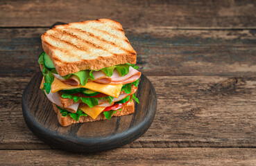 Club sandwich with ham, cheese, vegetables and grilled toast on a wooden, brown background. Side...