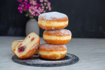 Freshly baked and garnished with powdered sugar German donuts - Berliner or Krapfen - on a white table. Black background. 