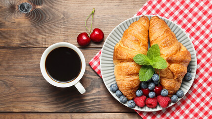 delicious croissants served with berries and mint leaf on the checkered towel with cup of coffee on the brown wooden table