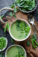 Creamy green pea soup with spinach in beige plates on a wooden tray on a gray table with a tablecloth.