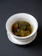 a white bowl with brewed tea leaves on a dark background. Close up, side view. Chinese tea, open leaves. vertical photo
