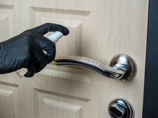 a man in black latex gloves sprays antiseptic on the door handle. Processing items to reduce the chance of infection with viruses