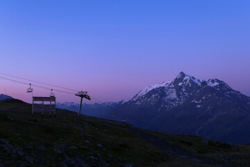Pink sunrise or sunset on mountain. Beautiful landscape with clear sky over the summit of a valley in alps. Ski resort with chairlift in the background.