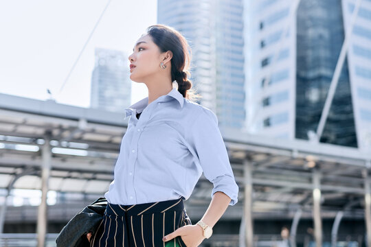 A beautiful Asian business woman is standing in a business district and looking ahead for something.