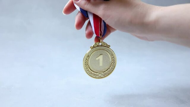 Hand holding winner or champion gold trophy medal on concrete stone grey background. Victory first place of competition. Winning or success concept