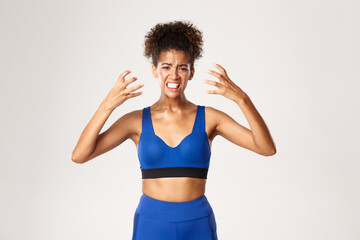 Fototapeta na wymiar Concept of sport and workout. Waist-up of distressed young african-american fitness woman in blue uniform, shaking hands and grimacing, looking frustrated, white background