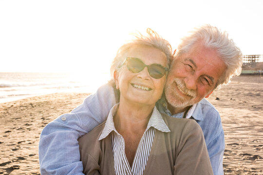 Portrait of couple of mature and old people enjoying summer at the beach looking to the camera smiling and having fun together with the sunset at the background. Two active seniors traveling outdoors.
