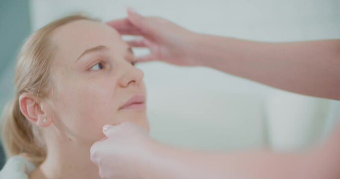 Close-up the face of a female client. A female cosmetologist is touching a face skin by fingers for the skin inspection.