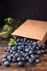 Ripe blueberries spilling out of a paper shopping bag on a dark wooden background.