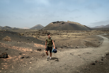 young man walks along a path in Masdache with "cuervo" volcano in the background. Lanzarote. Canary Islands