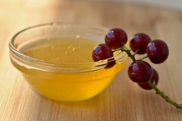 a sprig of red cherry berries dipped in a cup with honey on a wooden background