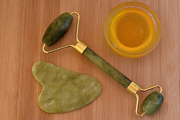 honey, scraper and jade gua sha massager on wooden surface