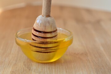 fresh honey flowing down a wooden spoon into a glass cup on a wooden surface