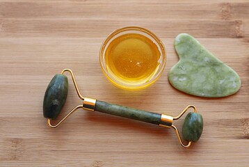 fresh honey, scraper and jade gua sha massager on wooden surface