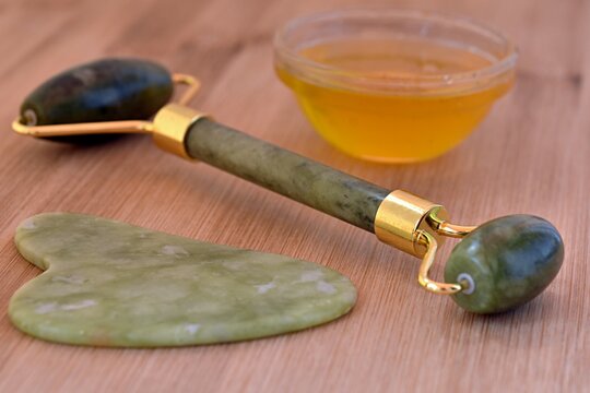 honey, scraper and jade gua sha massager on wooden surface