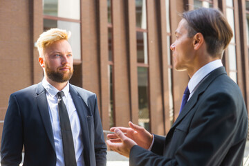 Confident businessman and his colleague in front of modern office building. Financial investors are talking outdoor. Banking and business.