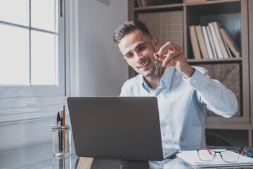 One happy caucasian man smiling and talking with clients online in video conference showing them their house keys. Busy worker using laptop or computer working..