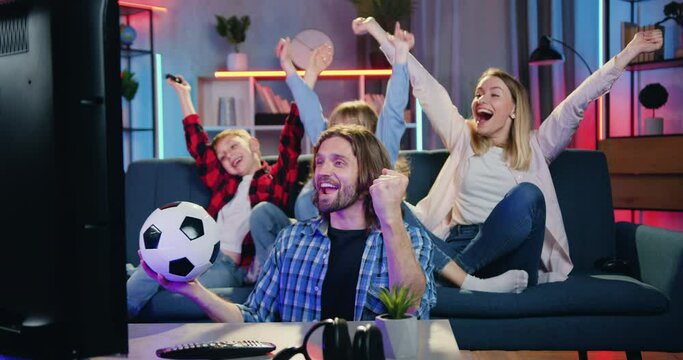 Attractive excited smiling happy family supporting favourite football team at home and screaming when players scored goal rejoycing from victory