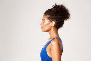 Fototapeta na wymiar Concept of workout and sport. Profile of young athletic girl in blue sports bra, looking left, standing against white background