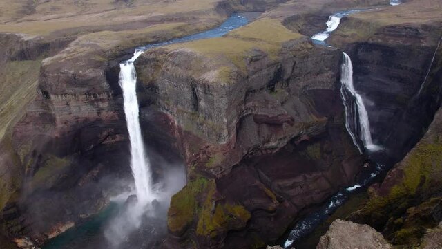 Wide aerial revolving shot around canyon with TWO waterfalls. Dramatic epic scenery, shot in Iceland. Steep cliffs and beautiful canyon.