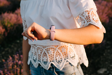 The girl looks at the fitness bracelet. The smart watch is worn on the girl's left hand. Silicone strap on a lilac-colored smart watch.