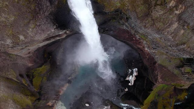 Rising birds eye view of a waterfall from above. Very interesting viewpoint, slowly rotating. Steep colorful cliffs.