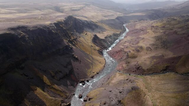 Epic aerial shot over a dramatic canyon with river landscape. Clouds moving creates moody feeling. Shot in Iceland.