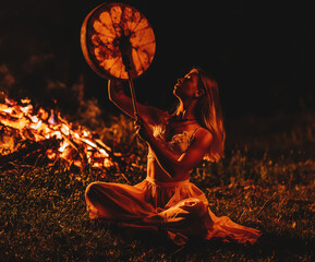 beautiful shamanic girl playing on shaman frame drum in the nature.