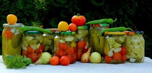 Preserves vegetables in glass jars on the table in summer garden. glass jars with various vegetables. Marinated food.Jars of pickled vegetables in the garden.