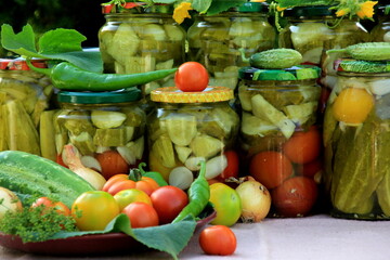 Preserves vegetables in glass jars on the table in summer garden. glass jars with various vegetables. Marinated food.Jars of pickled vegetables in the garden.