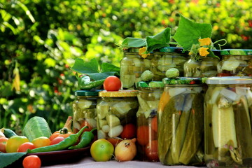 Preserves vegetables in glass jars on the table in summer garden. glass jars with various...