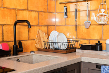 Modern kitchen design with ocher ceramic tiles and black metal mixer in the sink. 