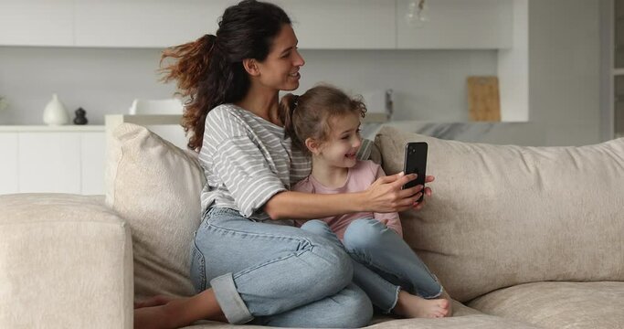 Happy two female generations family entertaining using funny mobile applications, playing games at home. Joyful young mother and small preteen kid daughter recording video, amusement with modern tech.