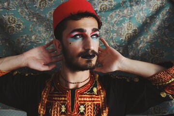 Portrait of queer young man with full face drag makeup & turkish anatolian ottoman traditional clothing with authentic patterns background *3 - obrazy, fototapety, plakaty