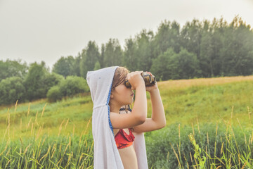 a child girl stands in a meadow and looks through binoculars