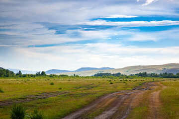 Dirt road in the Khakass steppe. Сountry road in the field. Picturesque clouds over the hills of Khakassia, Russia.