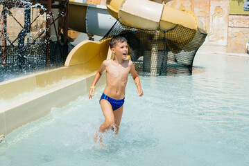 A happy boy of seven years old descends from the slides in the water park. Happy vacation vacation. Summer holidays and tourism.
