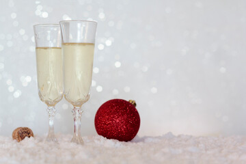 Two champagne glasses and red christmas ball on snow with bokeh background with copy space