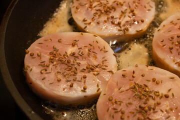 Hake fish fillets in the form of medallions sprinkled with spices cumin and coriander are fried in a frying pan.